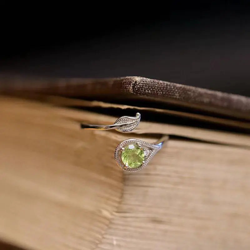 An olive green gemstone ring with a leaf and branch design on a wooden surface.