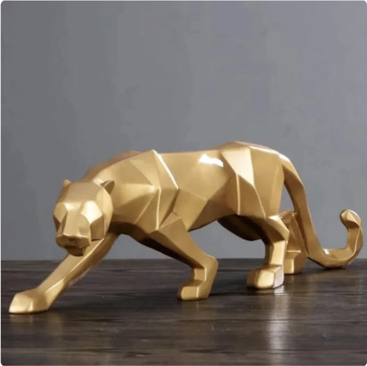 A gold-colored geometric cheetah figurine placed on a wooden surface against a neutral background.