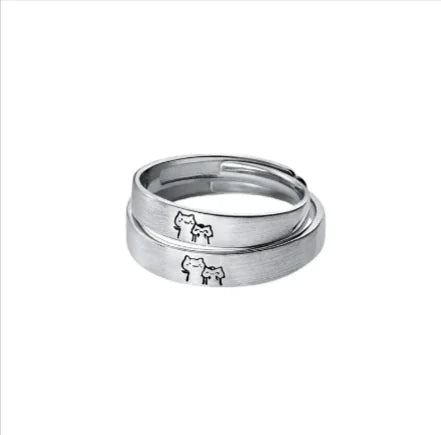 Two hands wearing adjustable couple rings with a cute kitten design on a white surface.