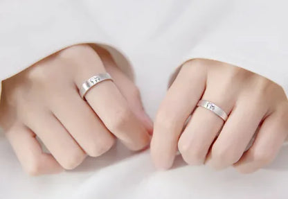 Two hands wearing adjustable couple rings with a cute kitten design on a white surface.