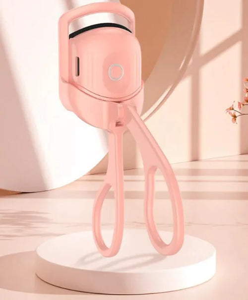 A portable electric heated eyelash curler in pink color, displayed on a stand, with a closed lid.