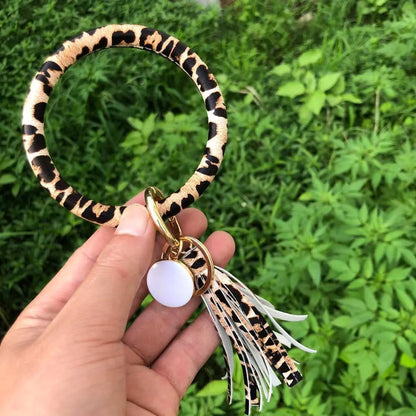 A hand holding a pure leather tassel pendant bracelet with a keyring attached, featuring a zebra-like print.