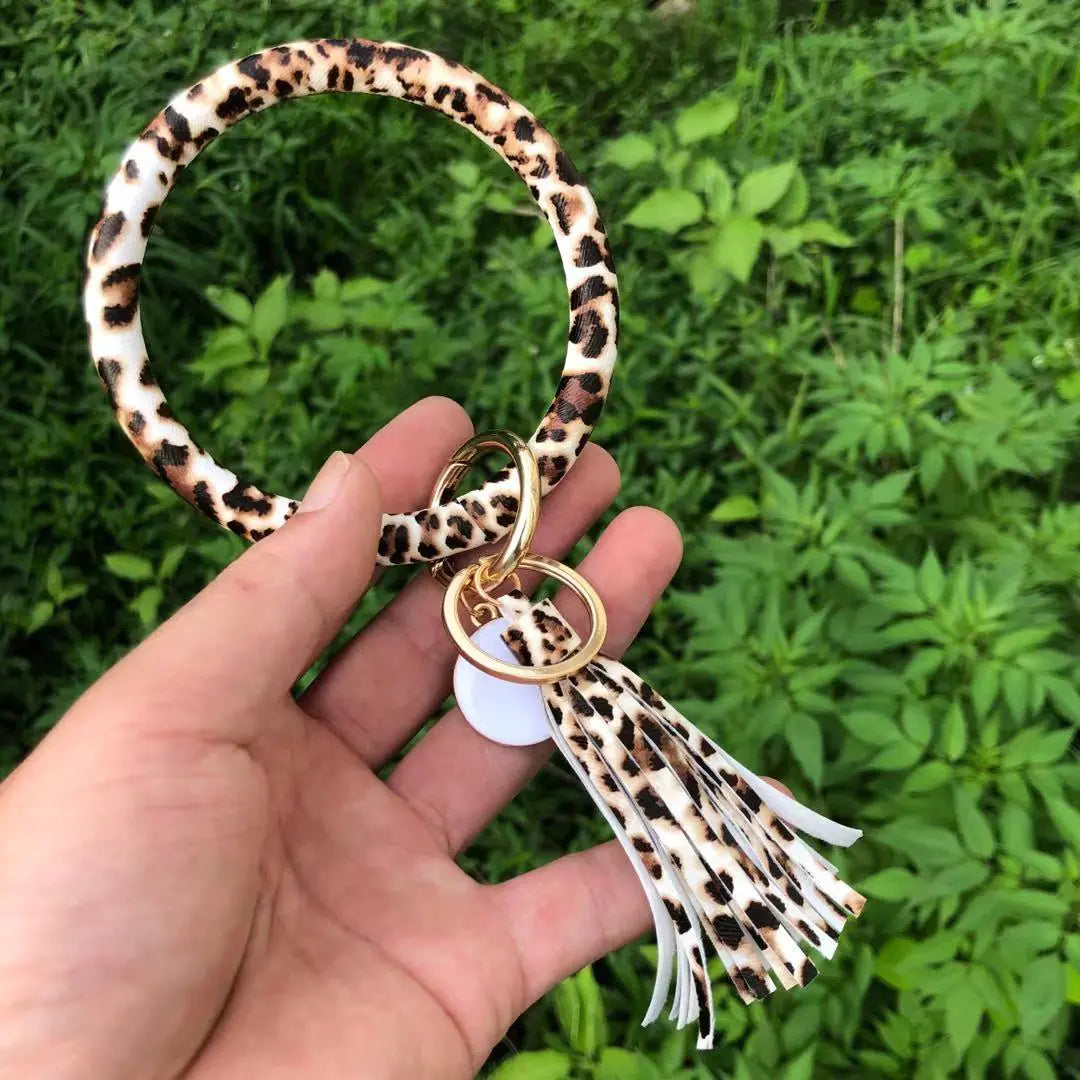 A hand holding a pure leather tassel pendant bracelet with a keyring attached, featuring a zebra-like print.