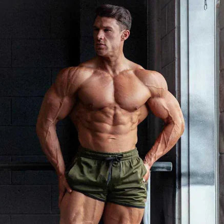 A man wearing green QuickFit sports shorts, showcasing his muscular physique.