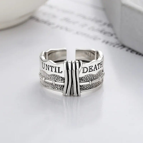 A silver ring with a distressed design and the text 'TIL DEATH' engraved on it, displayed against a light background.