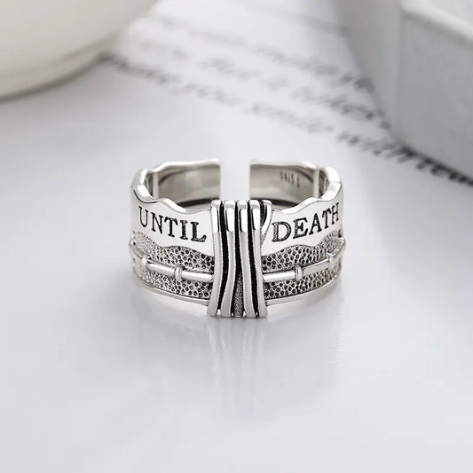 A silver ring with a distressed design and the text 'TIL DEATH' engraved on it, displayed against a light background.