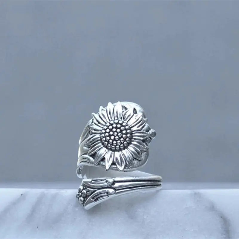 A silver ring with a daisy design, featuring an adjustable band and a prominent floral pattern on the top.