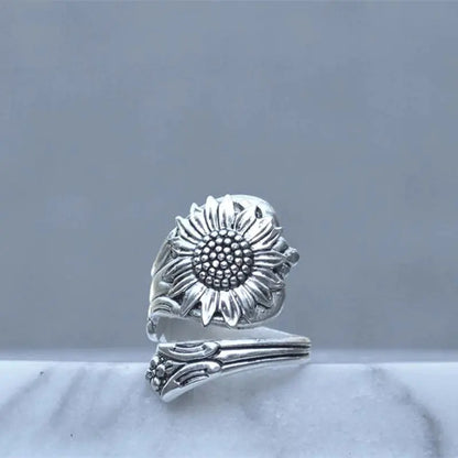 A silver ring with a daisy design, featuring an adjustable band and a prominent floral pattern on the top.
