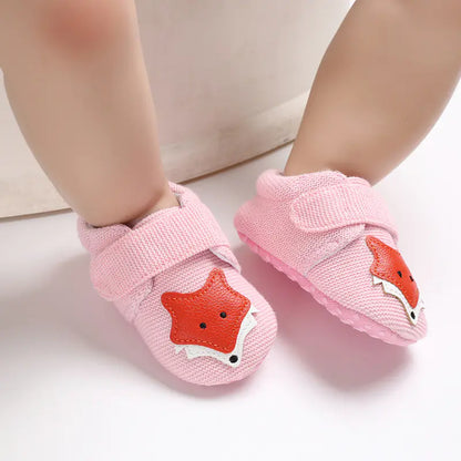A pair of gray baby shoes with a cartoon fox design on the top, displayed on a baby's feet.