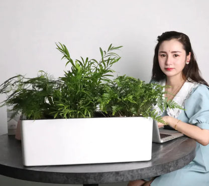 A woman sitting next to a round table with a space saving flower container on top, filled with green plants.