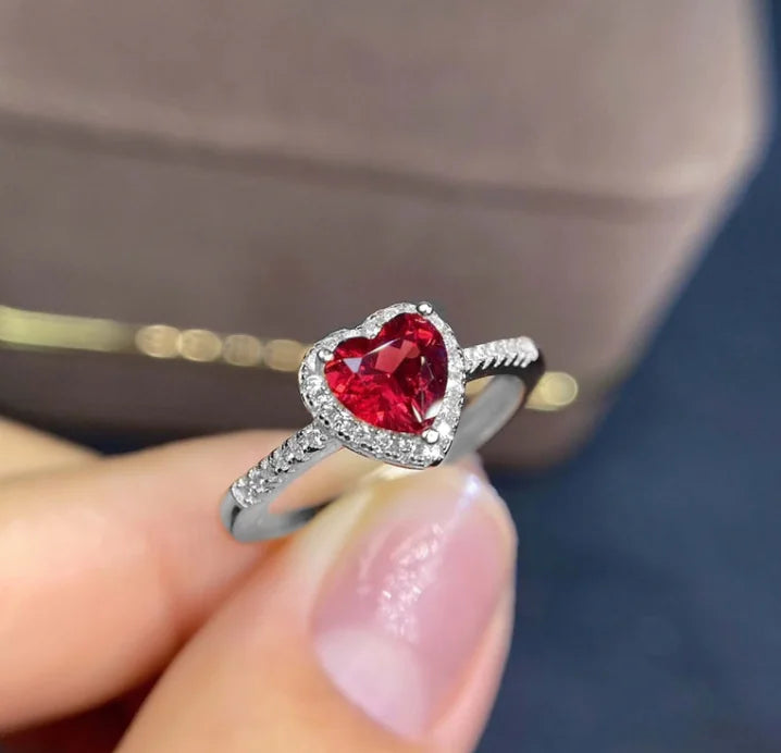 A heart-shaped diamond ring with a large central diamond surrounded by smaller diamonds on the band, held in a person's hand.