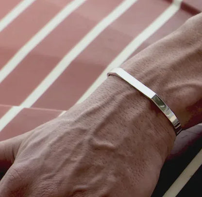 A stainless steel bracelet with a sleek, flat design, worn on a person's wrist.