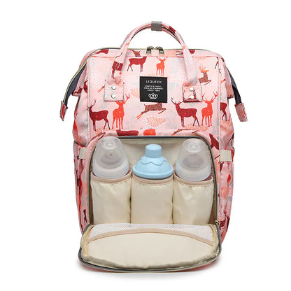 A pink mommy bag with a deer print, featuring multiple compartments including two baby bottles and a diaper, with a shoulder strap and a top handle.