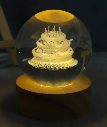A USB crystal ball night light glowing with a warm light, resembling a birthday cake with candles on top, placed on a wooden surface.