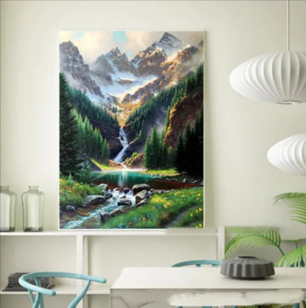 A diamond painting kit depicting a landscape with a waterfall, mountains, and a clear sky being assembled on a table.