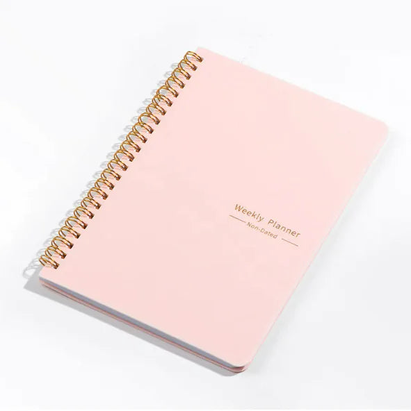 A pink weekly schedule notebook with a spiral binding and the text 'Weekly Planner' printed on the cover.