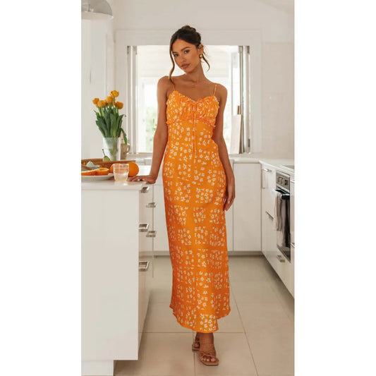 A woman standing in a kitchen wearing a sleeveless, v-neck, backless orange and blue floral print dress.