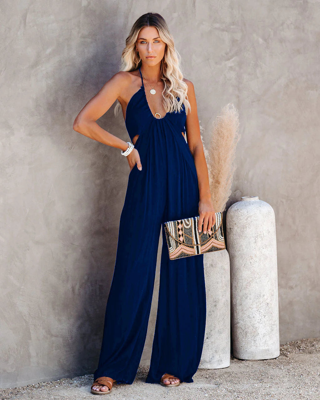 A woman wearing a navy blue U-Neck Backless Wide-Leg Jumpsuit standing on the beach.