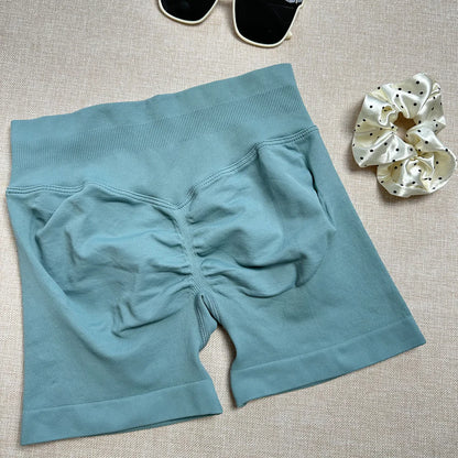 A pair of blue yoga shorts laid flat on a surface, with a high-waist fit and a small amount of stretch fabric visible.