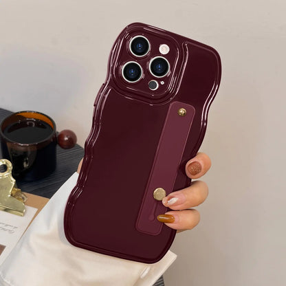 A black silicone phone case for iPhone 16 Pro Max with a simple curvy wave frame design and an adjustable wrist strap kickstand, held in a person's hand.