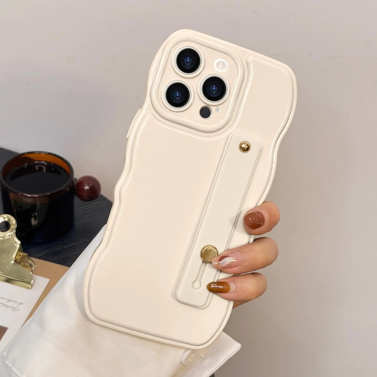 A black silicone phone case for iPhone 16 Pro Max with a simple curvy wave frame design and an adjustable wrist strap kickstand, held in a person's hand.