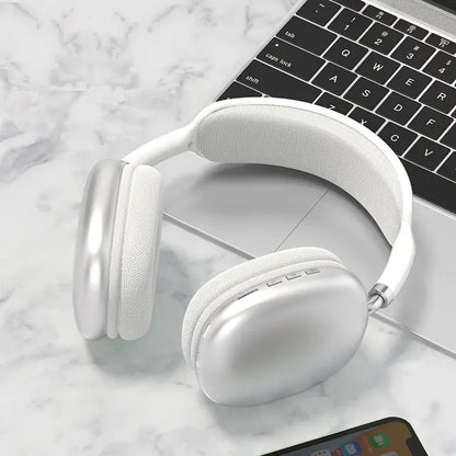 A pair of white P9 wireless Bluetooth headphones with a microphone, resting on a marble surface next to a smartphone and a laptop.