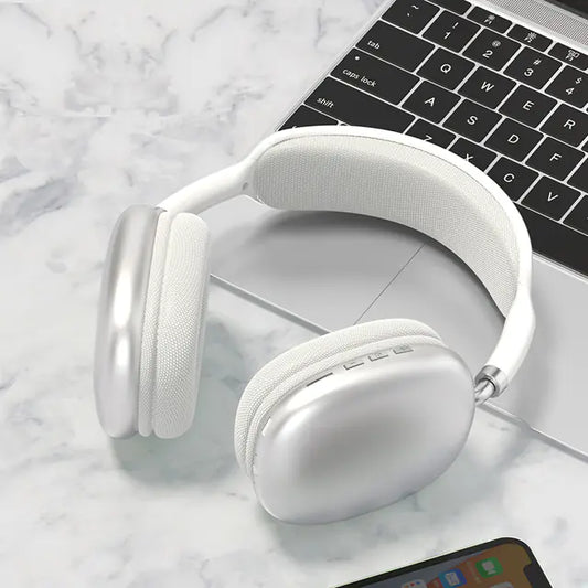 A pair of white P9 wireless Bluetooth headphones with a microphone, resting on a marble surface next to a smartphone and a laptop.